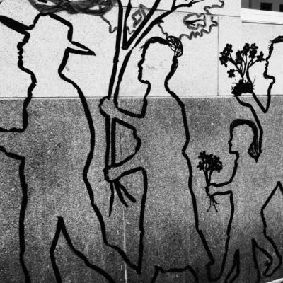 An outline of a family on a concrete wall. They appear to be walking towards the left and are each holding various plants.