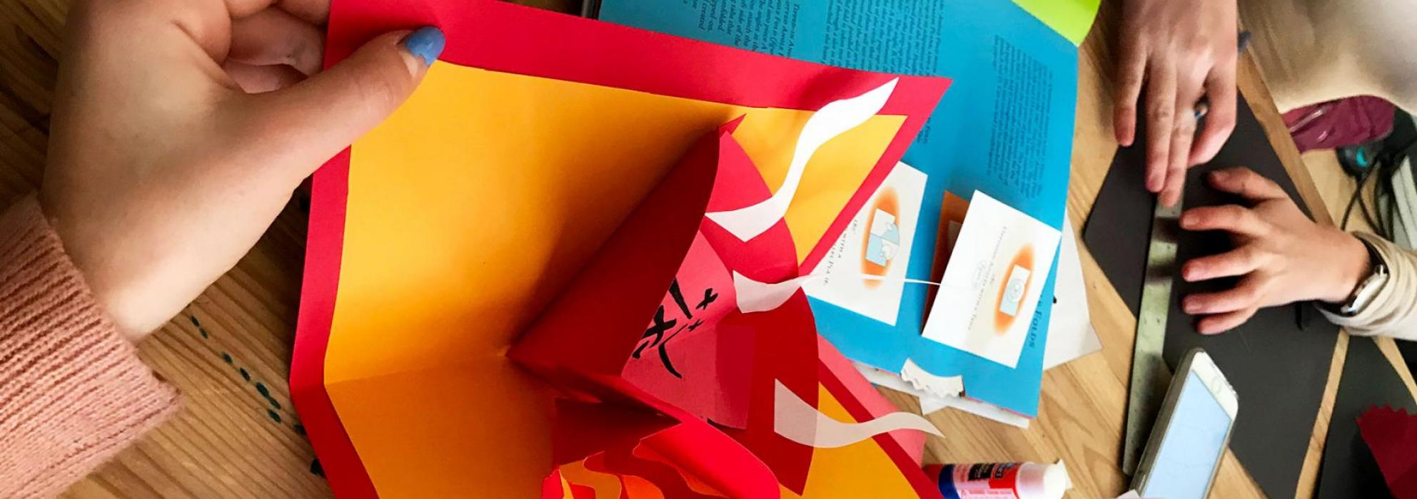 An up close image of a student opening a small booklet made from red and yellow paper.