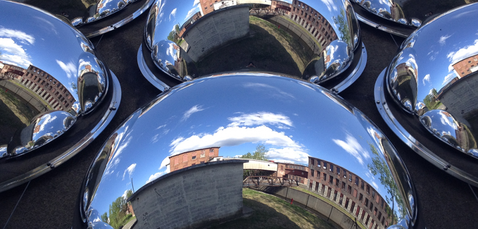 Close-up of multiple reflective metal domes mirroring buildings, and clouds.  