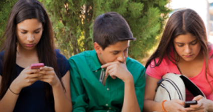 Three teens sit side by side, looking at their phones