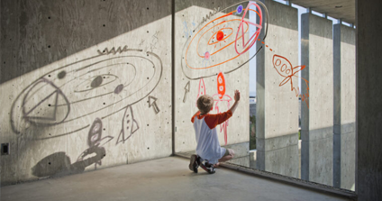 A child draws on a glass window with red marker