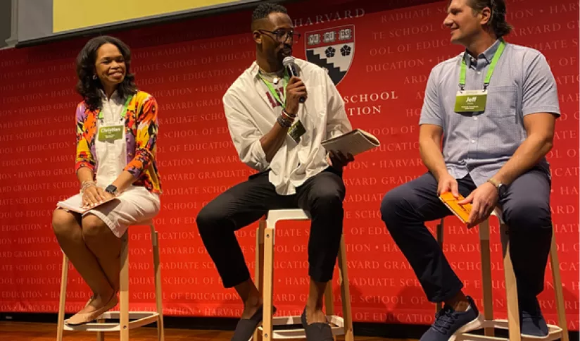 Three adults speak onstage at a conference