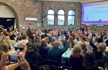 A group of adults throw paper airplanes at a conference